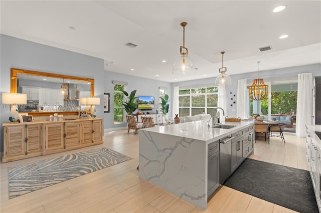 kitchen featuring sink, light stone counters, decorative light fixtures, a kitchen island with sink, and light wood-type flooring