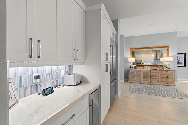 kitchen with built in fridge, light wood-type flooring, light stone countertops, and white cabinets