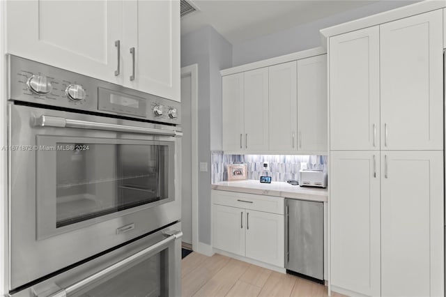 kitchen with white cabinetry, appliances with stainless steel finishes, light hardwood / wood-style floors, and backsplash