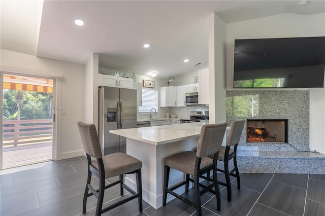 kitchen with a breakfast bar, kitchen peninsula, appliances with stainless steel finishes, a fireplace, and white cabinets