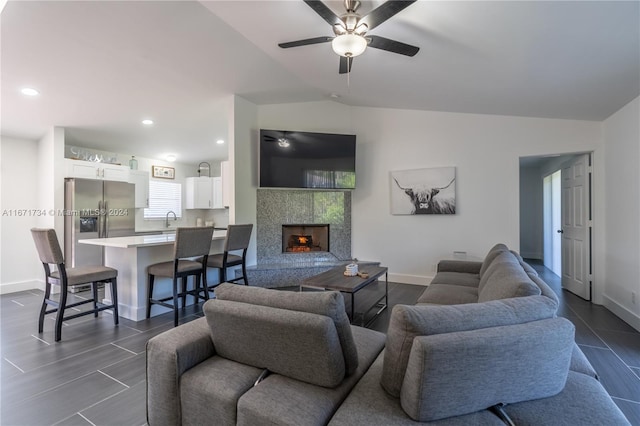 living room with ceiling fan, a tile fireplace, sink, and vaulted ceiling