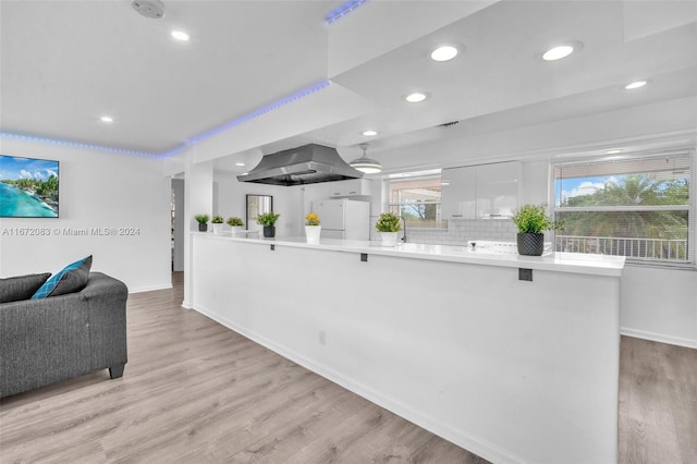 kitchen with white refrigerator, white cabinets, island exhaust hood, kitchen peninsula, and light hardwood / wood-style flooring