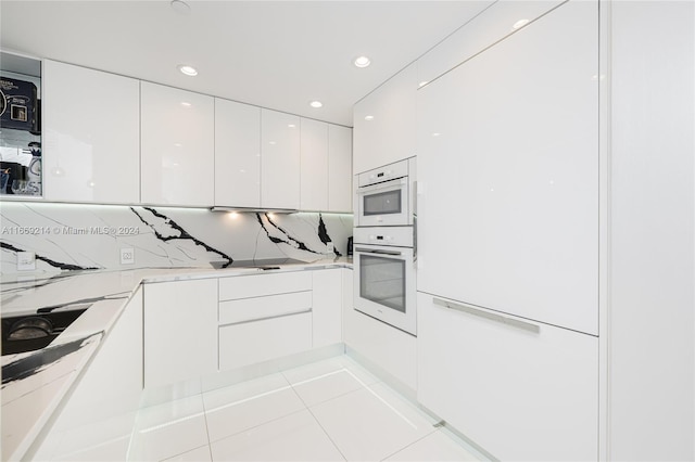 kitchen featuring white oven, light tile patterned floors, tasteful backsplash, and white cabinetry