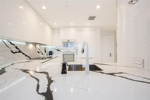 kitchen with white cabinetry, white double oven, light stone countertops, black electric stovetop, and sink