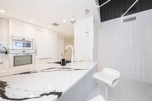 kitchen featuring white cabinetry, hanging light fixtures, white double oven, light tile patterned floors, and light stone countertops