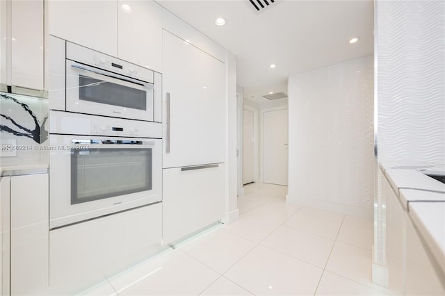 kitchen with light stone counters, white cabinets, stainless steel double oven, and light tile patterned floors