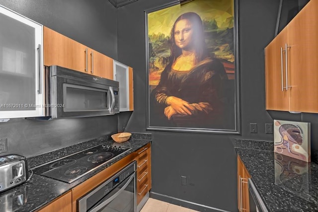 kitchen with dark stone counters, appliances with stainless steel finishes, and light tile patterned floors