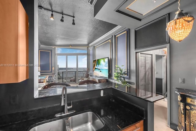 kitchen with pendant lighting, a textured ceiling, crown molding, dark stone counters, and sink