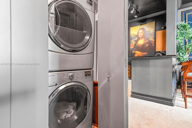 clothes washing area with carpet flooring, stacked washer / drying machine, and rail lighting