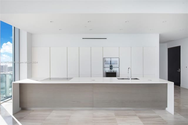 kitchen with a wall of windows, a large island with sink, sink, and white cabinetry