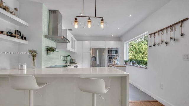 kitchen featuring pendant lighting, white cabinets, kitchen peninsula, wall chimney exhaust hood, and appliances with stainless steel finishes