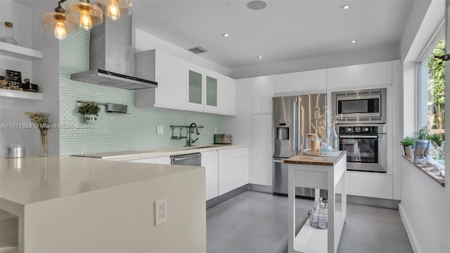 kitchen with pendant lighting, stainless steel appliances, white cabinetry, and wall chimney range hood