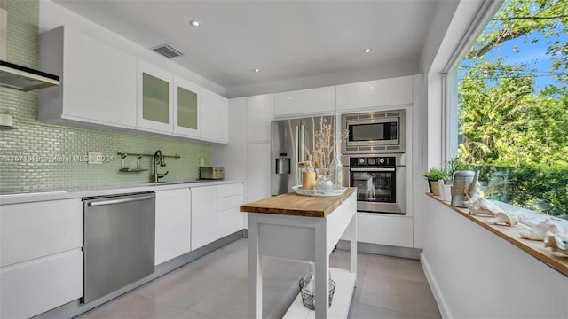 kitchen featuring tasteful backsplash, sink, white cabinets, wall chimney exhaust hood, and appliances with stainless steel finishes