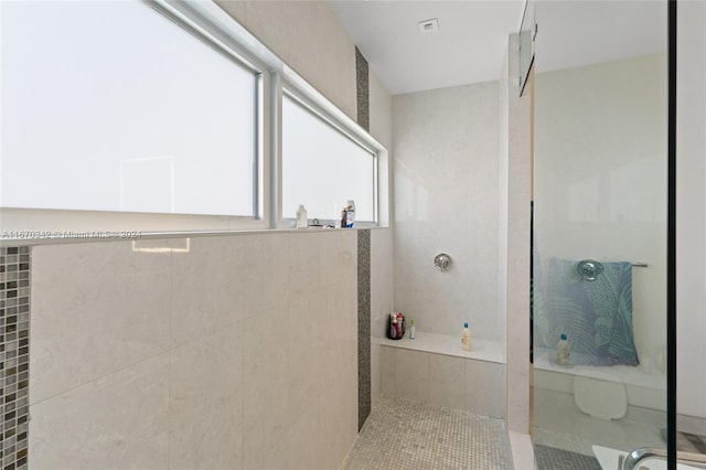 bathroom with a tile shower, tile patterned flooring, and tile walls