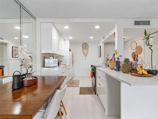 kitchen with white cabinetry, light tile patterned floors, white appliances, and a textured ceiling