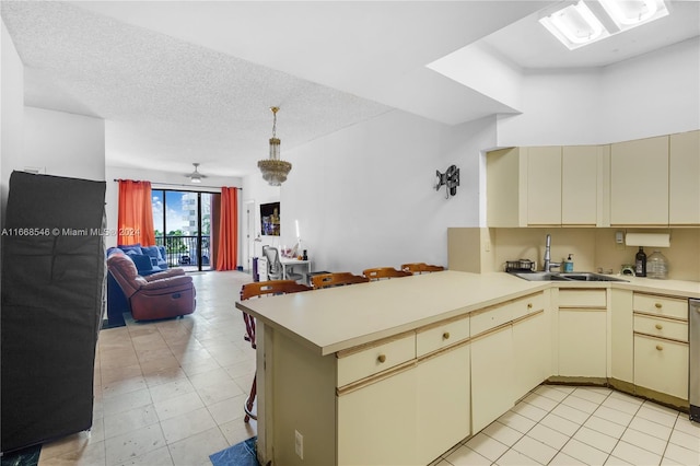 kitchen with a textured ceiling, kitchen peninsula, cream cabinets, and sink