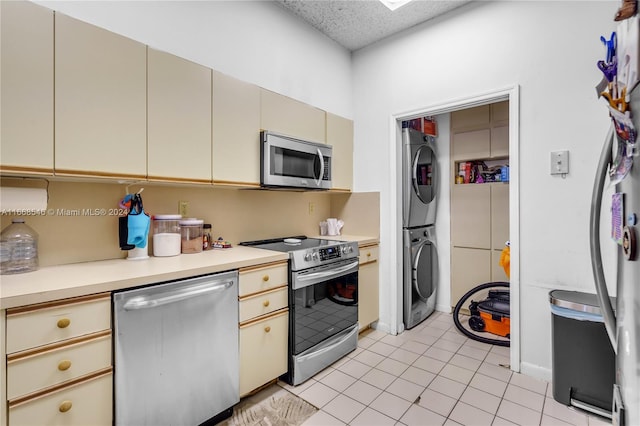 kitchen with a skylight, light tile patterned floors, stacked washer and clothes dryer, cream cabinets, and stainless steel appliances