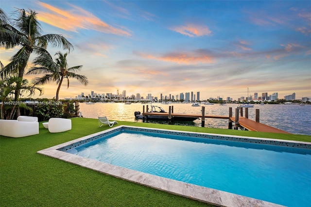 pool at dusk with a water view, a yard, and a dock