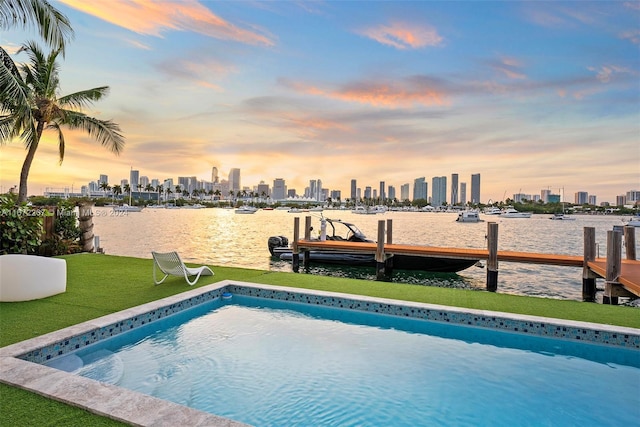 pool at dusk featuring a water view, a yard, and a dock