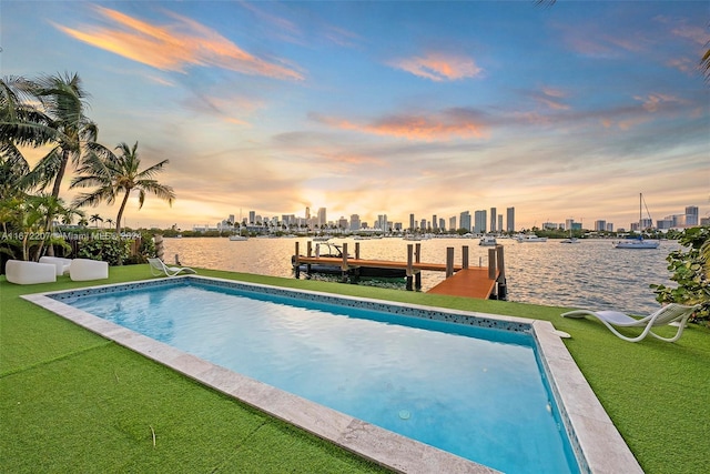 pool at dusk featuring a water view, a yard, and a dock