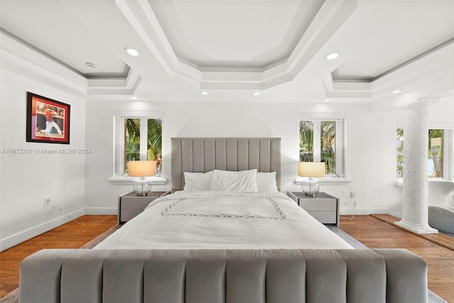 bedroom featuring a tray ceiling, multiple windows, light hardwood / wood-style flooring, and decorative columns