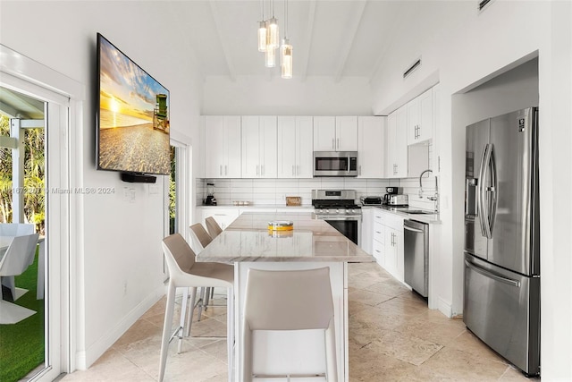 kitchen with appliances with stainless steel finishes, decorative light fixtures, white cabinetry, a kitchen island, and a breakfast bar area