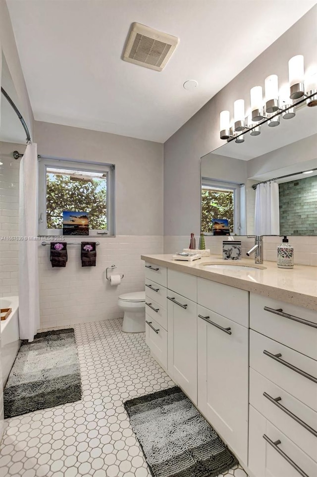 full bathroom with tile patterned flooring, vanity, tile walls, toilet, and shower / bath combo with shower curtain