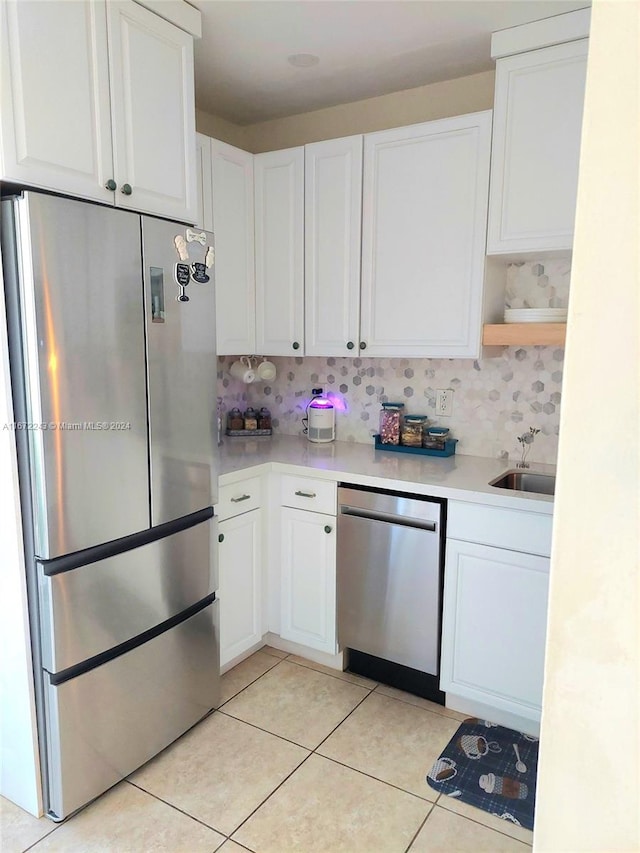 kitchen with sink, light tile patterned flooring, backsplash, stainless steel appliances, and white cabinets