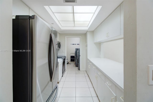 kitchen with light tile patterned floors, light countertops, white cabinets, washer and clothes dryer, and stainless steel appliances