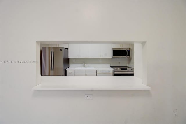 kitchen featuring a sink, light countertops, appliances with stainless steel finishes, a peninsula, and white cabinetry