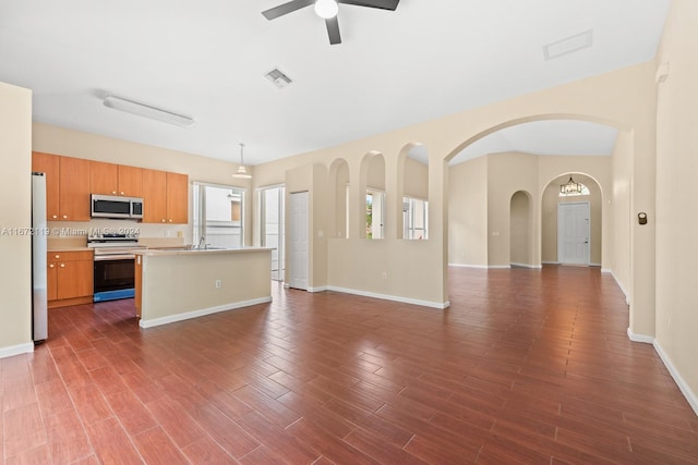 kitchen featuring appliances with stainless steel finishes, an island with sink, dark hardwood / wood-style flooring, ceiling fan, and decorative light fixtures