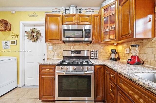 kitchen featuring light tile patterned floors, light stone countertops, appliances with stainless steel finishes, tasteful backsplash, and washer / dryer