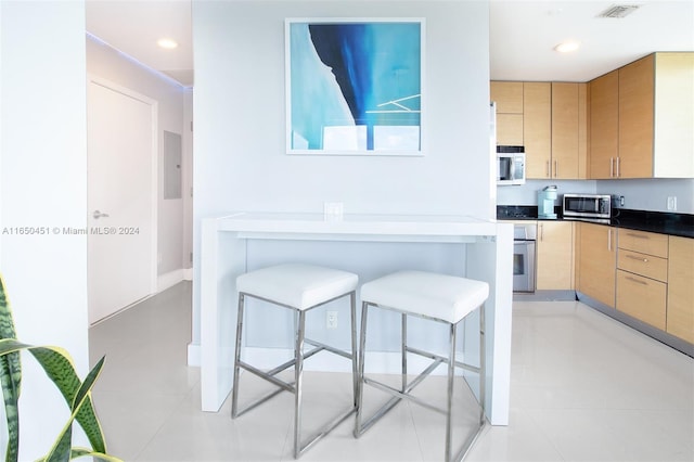 kitchen featuring a breakfast bar area, appliances with stainless steel finishes, light brown cabinetry, and light tile patterned floors