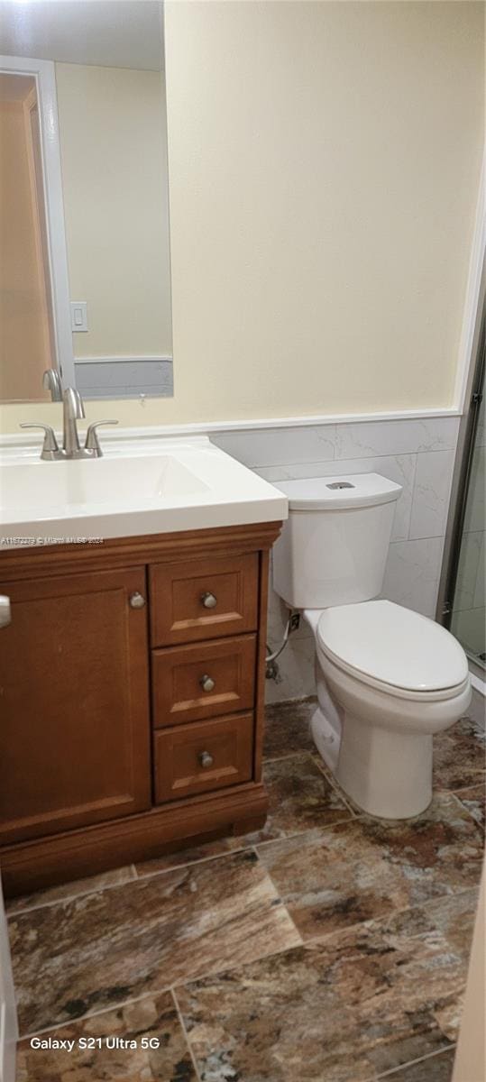 bathroom featuring vanity, toilet, tile walls, and walk in shower