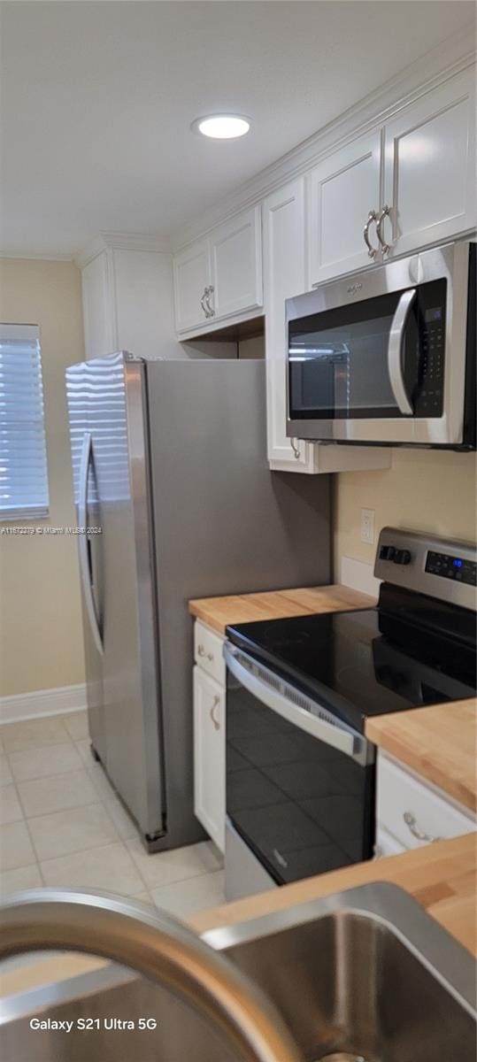 kitchen with white cabinetry, light tile patterned floors, butcher block counters, and appliances with stainless steel finishes