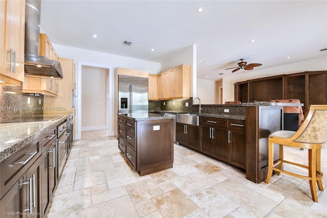 kitchen with decorative backsplash, a breakfast bar area, a kitchen island, wall chimney exhaust hood, and sink