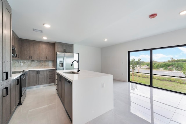 kitchen with sink, backsplash, an island with sink, light tile patterned flooring, and appliances with stainless steel finishes