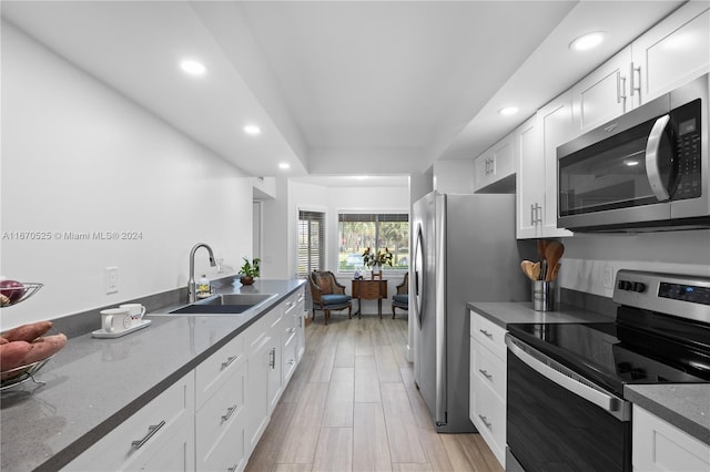 kitchen with appliances with stainless steel finishes, dark stone counters, sink, light hardwood / wood-style flooring, and white cabinets