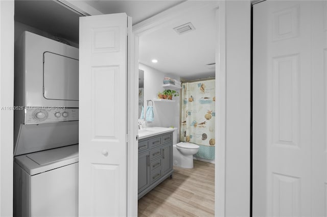 bathroom featuring walk in shower, stacked washer / dryer, toilet, vanity, and hardwood / wood-style flooring