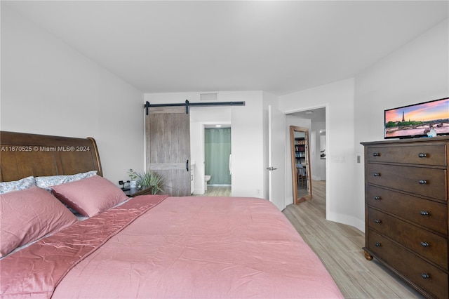 bedroom with a barn door and light hardwood / wood-style flooring