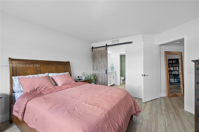 bedroom with connected bathroom, light hardwood / wood-style floors, and a barn door