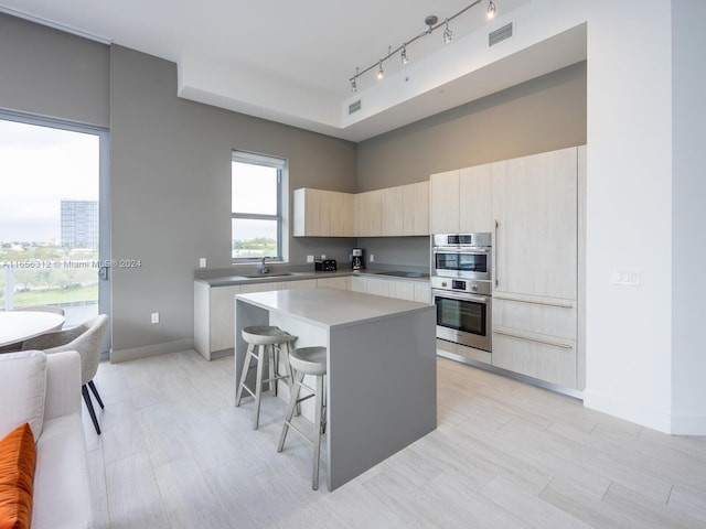 kitchen with black electric stovetop, a center island, sink, a kitchen bar, and double oven