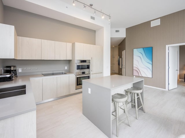 kitchen featuring sink, a kitchen island, black electric cooktop, double oven, and a kitchen breakfast bar