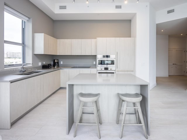 kitchen featuring black electric stovetop, a center island, sink, a breakfast bar area, and double oven