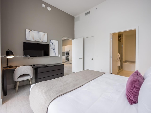 bedroom with connected bathroom, a towering ceiling, and light wood-type flooring