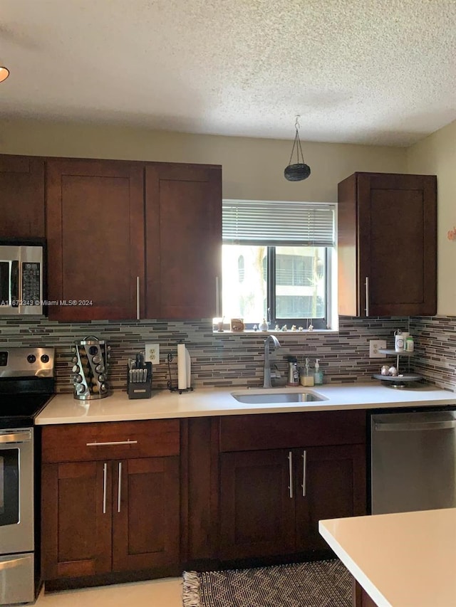 kitchen featuring appliances with stainless steel finishes, backsplash, a textured ceiling, dark brown cabinetry, and sink