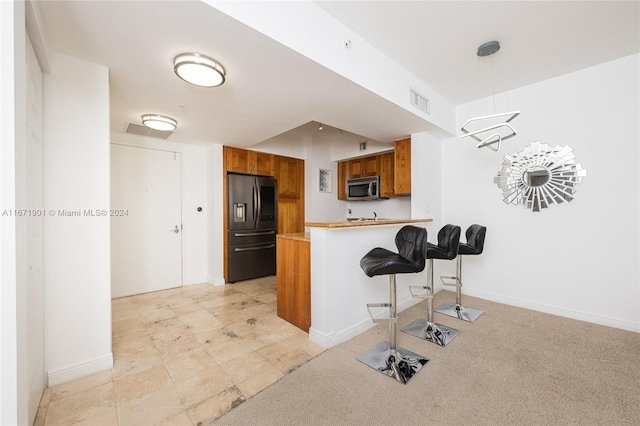 kitchen with light carpet, kitchen peninsula, decorative light fixtures, a kitchen breakfast bar, and refrigerator with ice dispenser