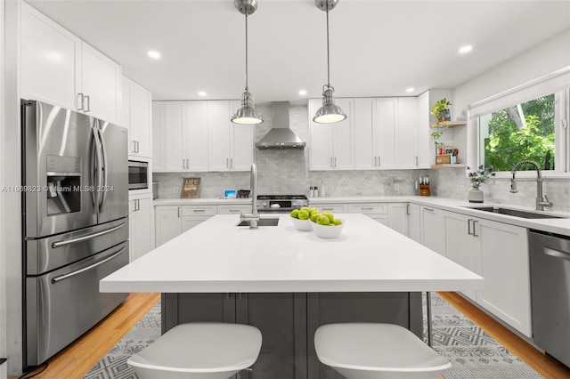 kitchen featuring wall chimney range hood, sink, a center island, white cabinetry, and stainless steel appliances