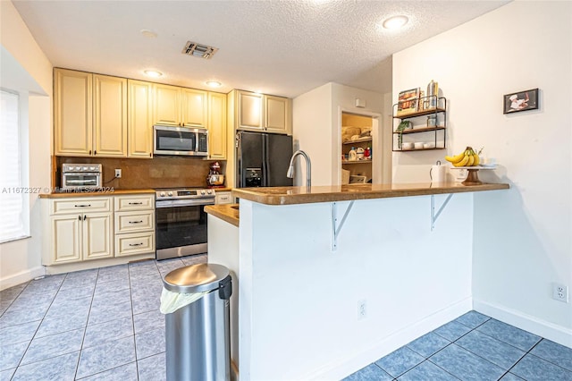 kitchen featuring a breakfast bar area, light tile patterned floors, a textured ceiling, kitchen peninsula, and stainless steel appliances