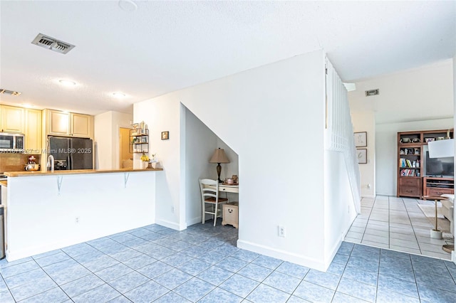 2913 Myrtle Oak Cir, Davie, FL 33328 - kitchen with black fridge, stainless steel microwave, light tile patterned floors, tasteful backsplash, and cream cabinets